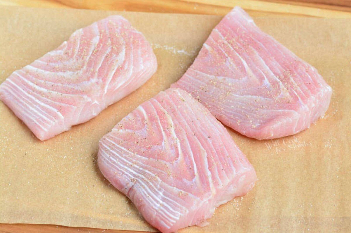 three seasoned uncooked filets of mahi mahi on the parchment paper.