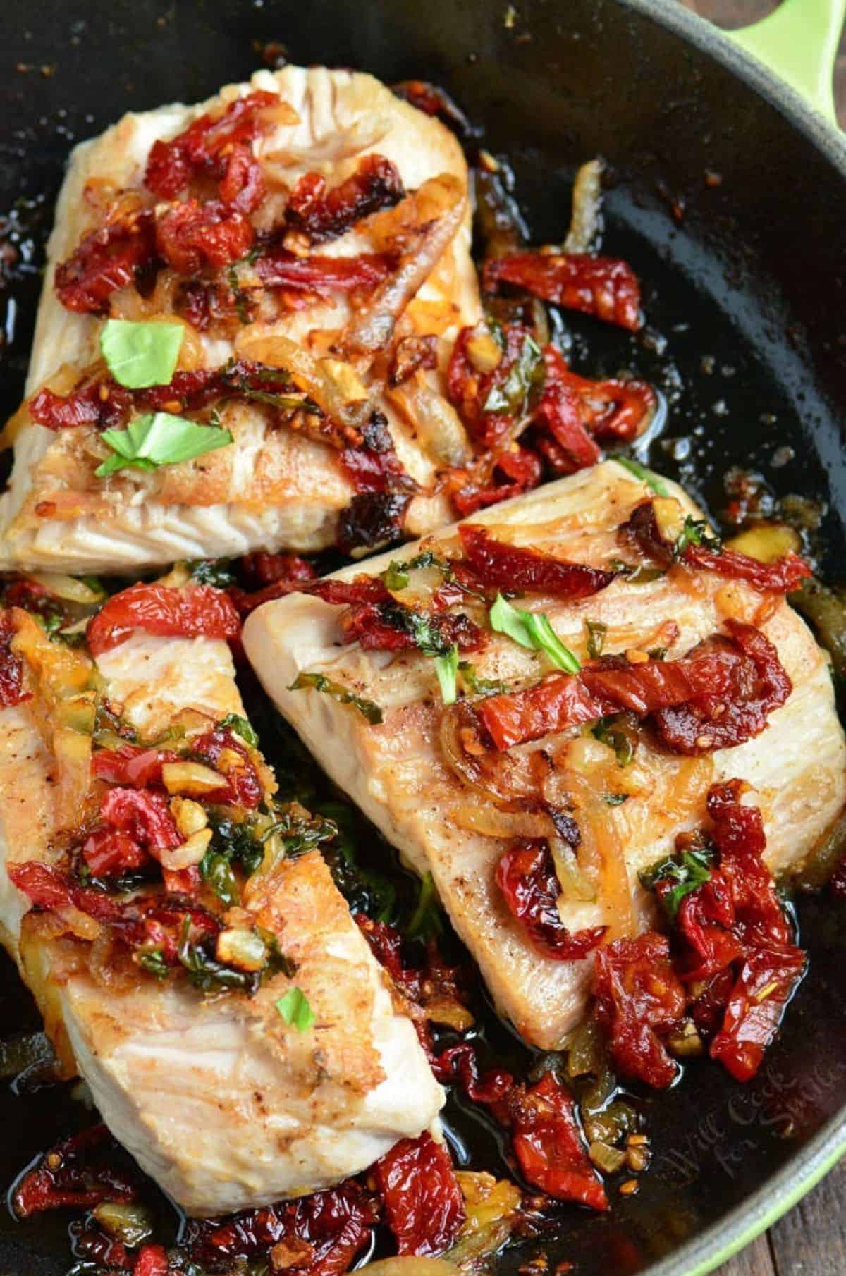 Three mahi mahi filets in the skillet with a sun dried tomato basil topping.