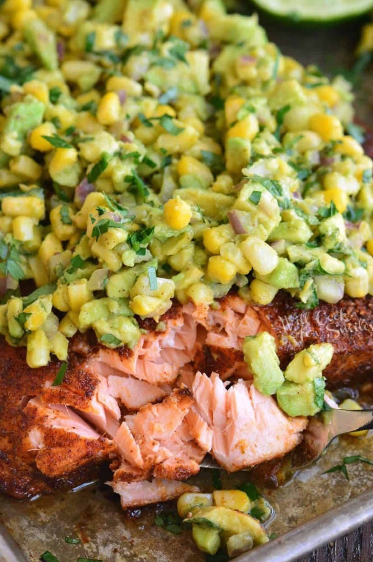 flaked baked salmon on a fork next to salmon filet with avocado corn topping.