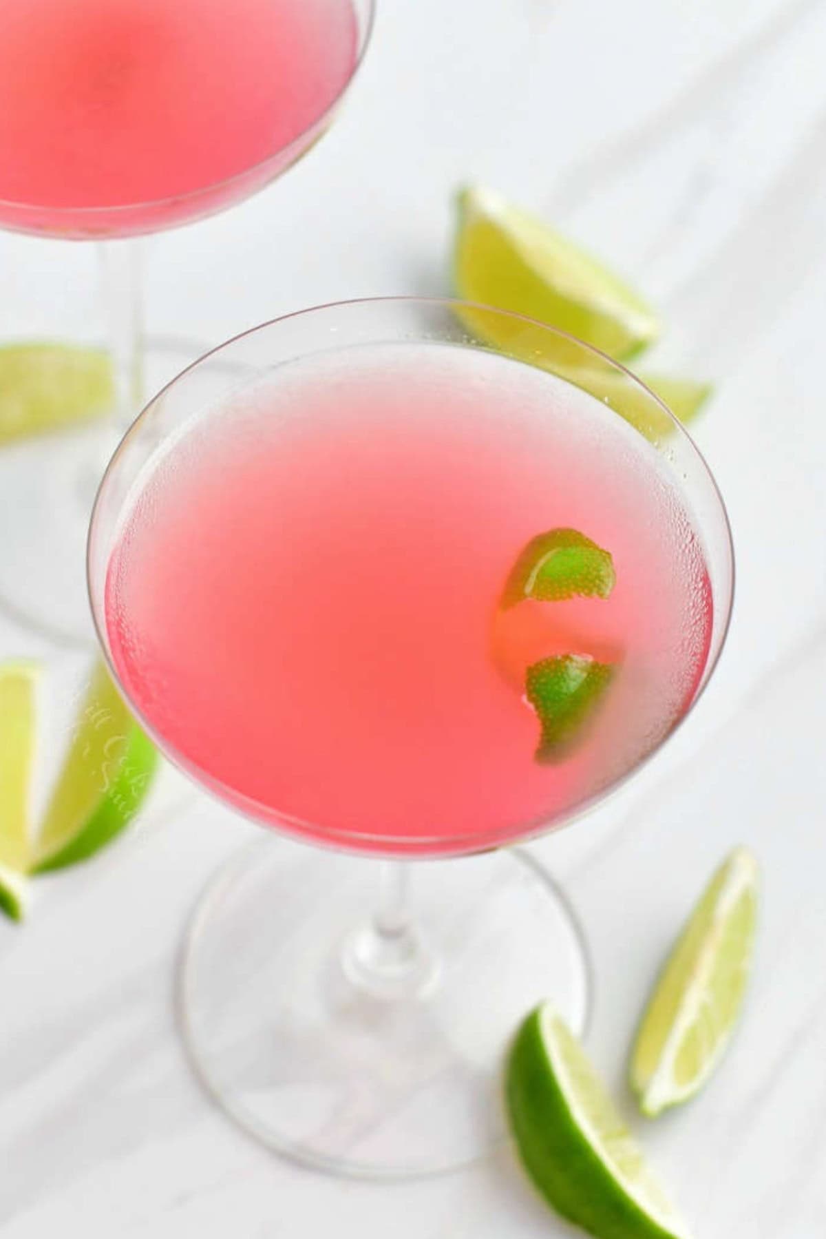 light pink cosmopolitan cocktail in a martini glass with lime wedges around.
