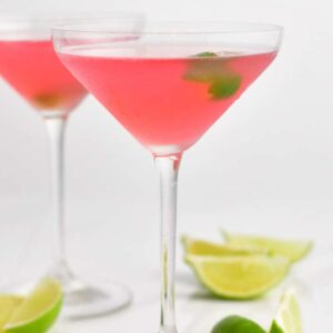 two tall martini glasses filled with cosmopolitan cocktail and lime twist.