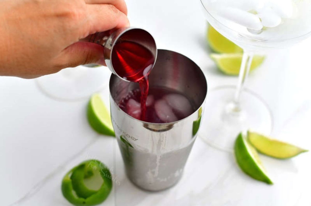 pouring cranberry juice into the cocktail shaker next to chilling martini glass.