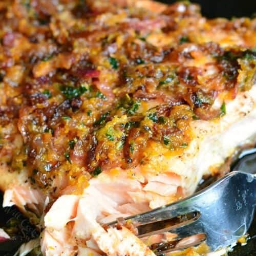 cutting into the grilled salmon in a skillet with a fork and citrus sauce on top.