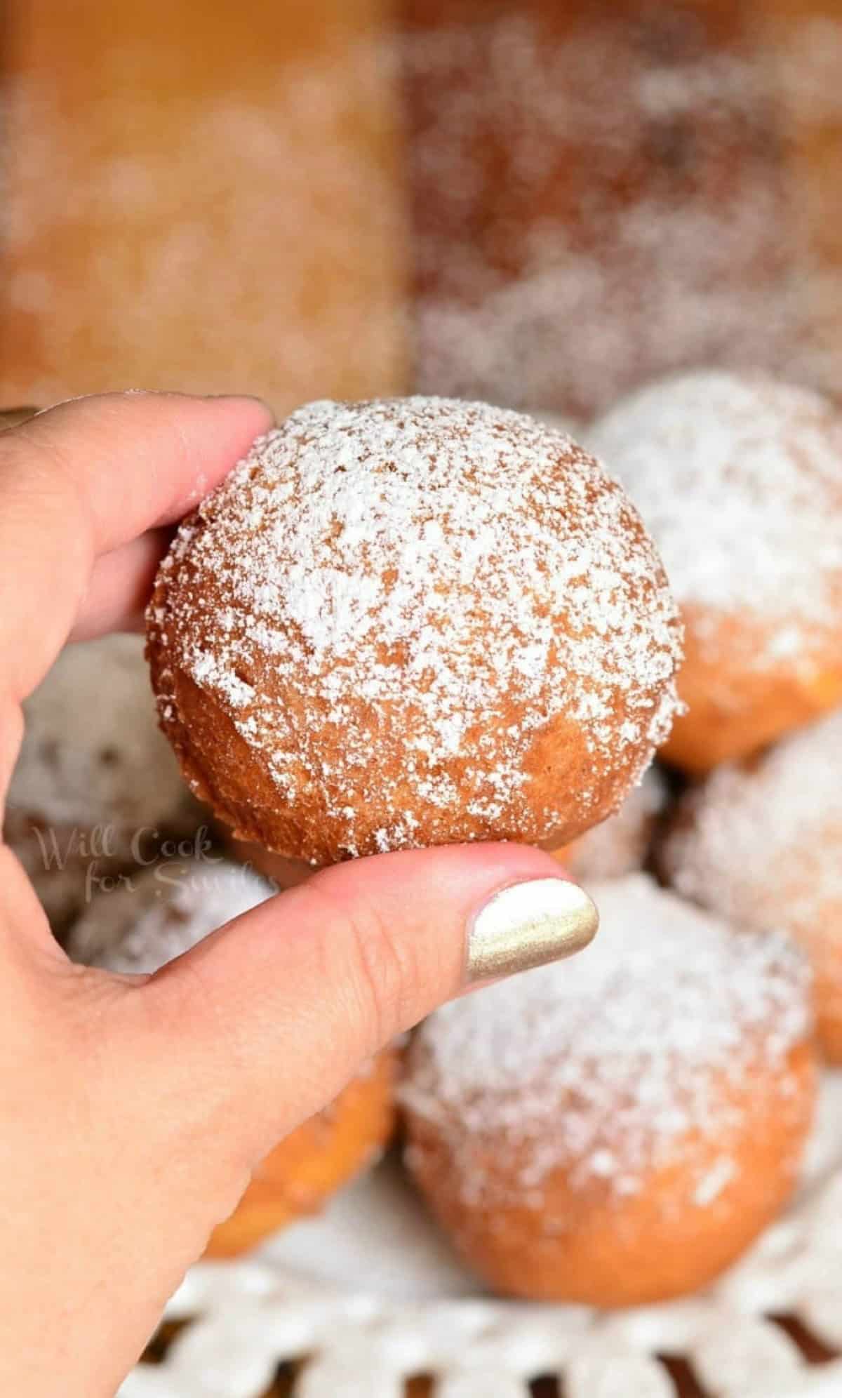 holding one doughnut hole over the plate of more.