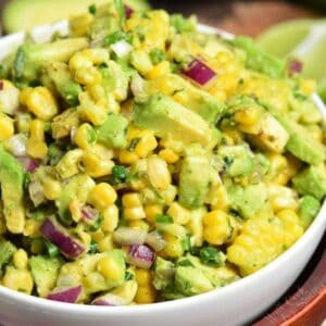 Avocado Corn Salad in a bowl with avocado sliced in half in the background.