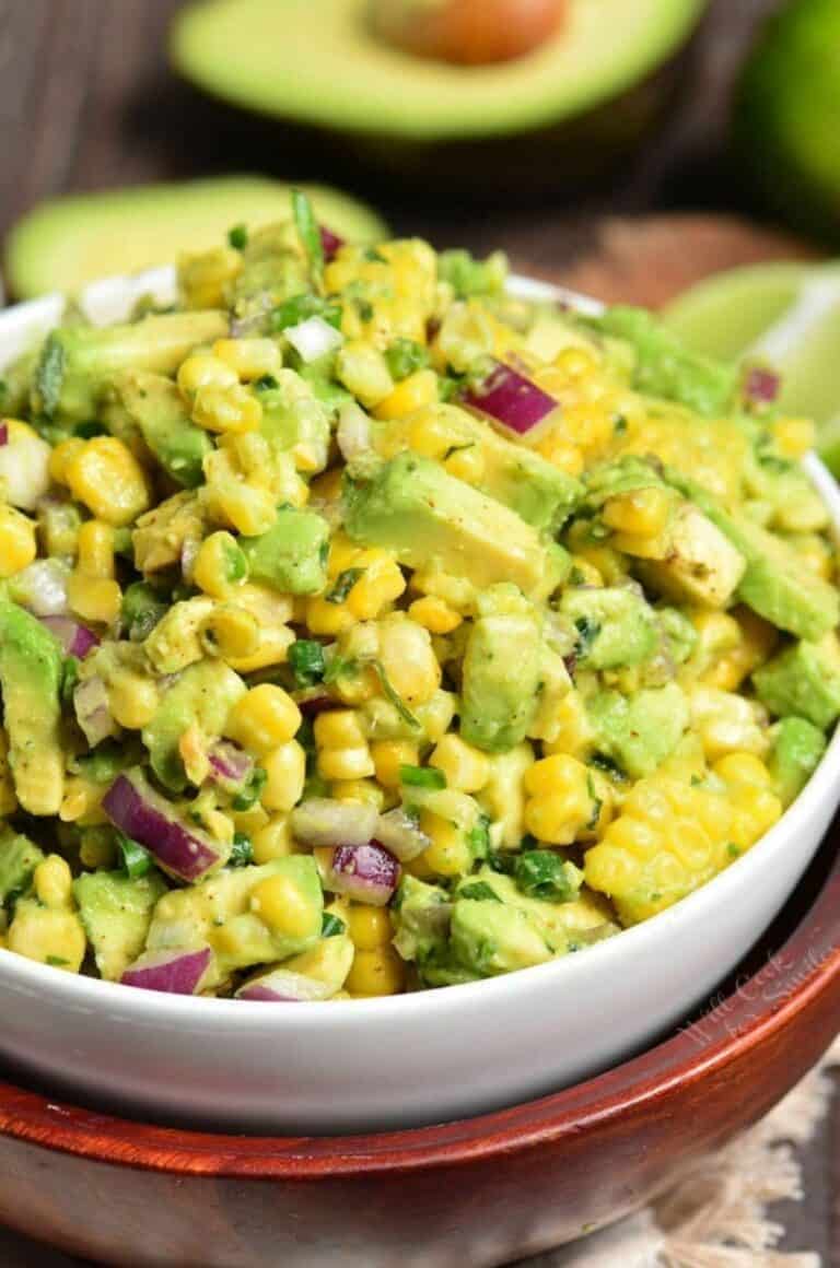 Avocado Corn Salad in a bowl with avocado sliced in half in the background.