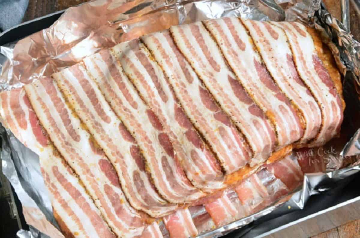 uncooked whole beef brisket seasoned and wrapped in bacon in aluminum paper in roasting pan.