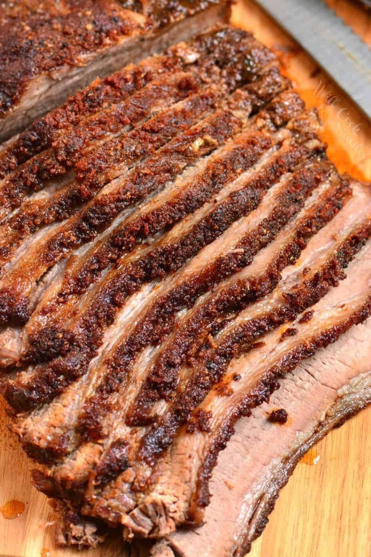 sliced dry rubbed juicy beef brisket laying on the cutting board next to a knife.