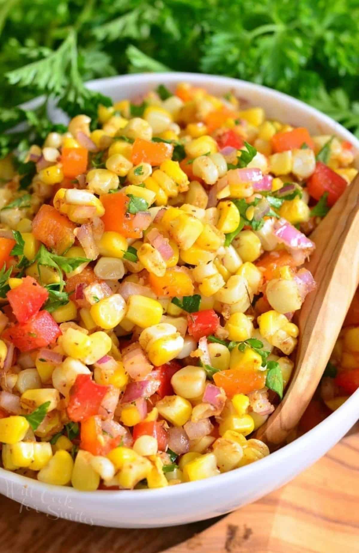Cajun corn salad in a bowl with fresh herbs next to it.