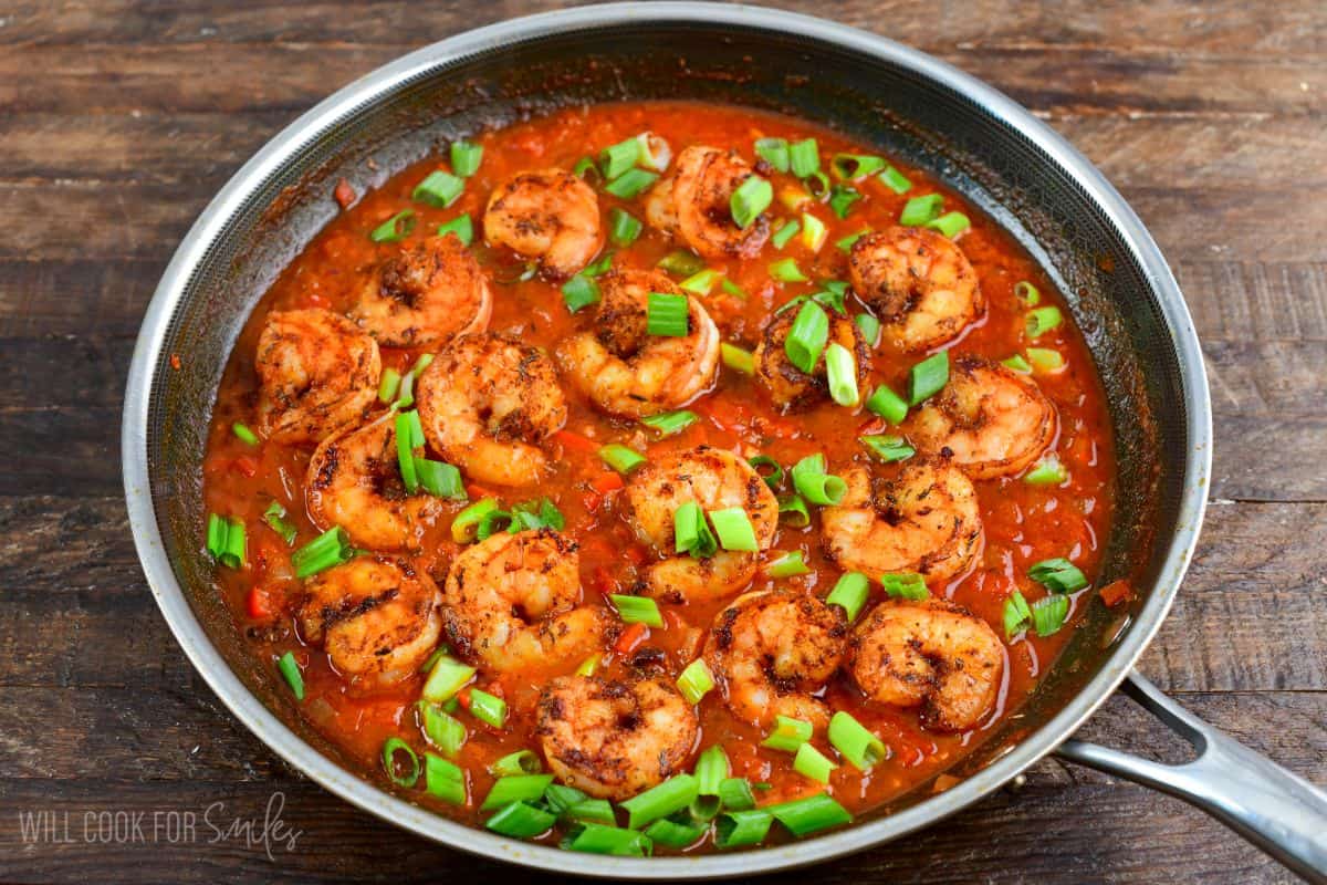 Cajun shrimp in a pan with green onions on a wood surface.