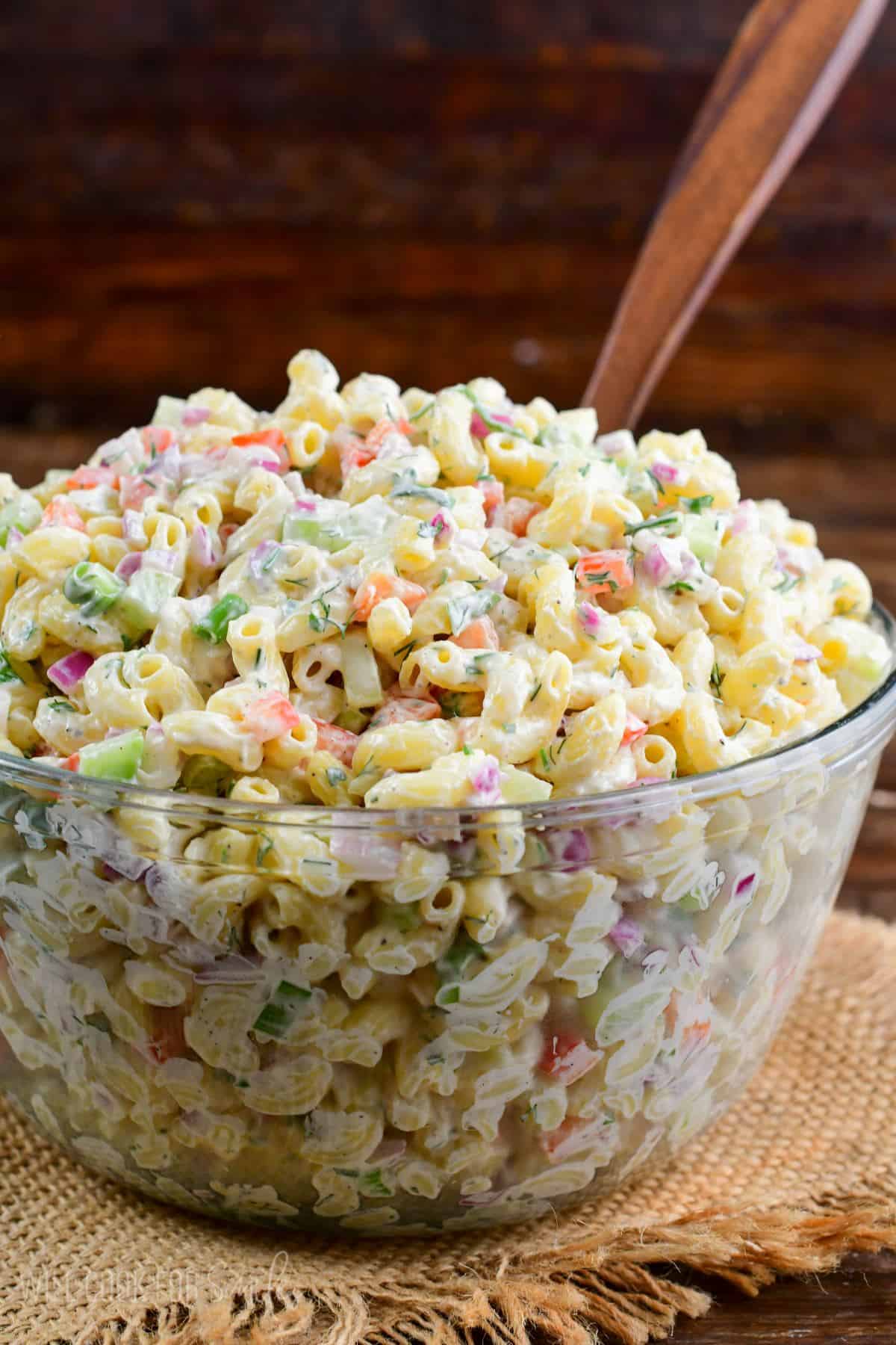 macaroni salad in a big glass bowl with a wooden spoon.