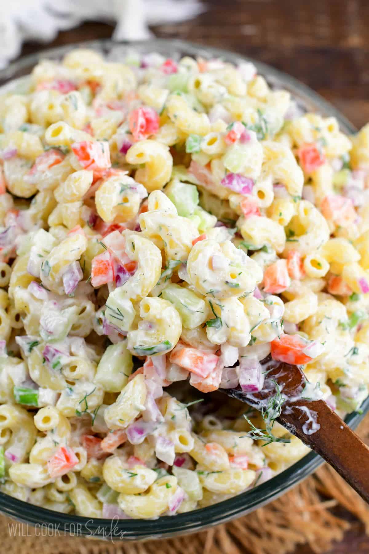 macaroni salad in a serving bowl with a wooden spoon scooping some out.