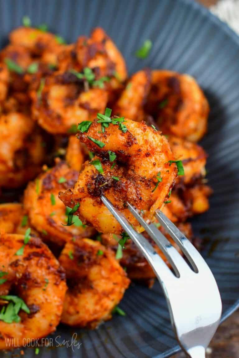 holding one blackened shrimp on a fork in front on a bowl.