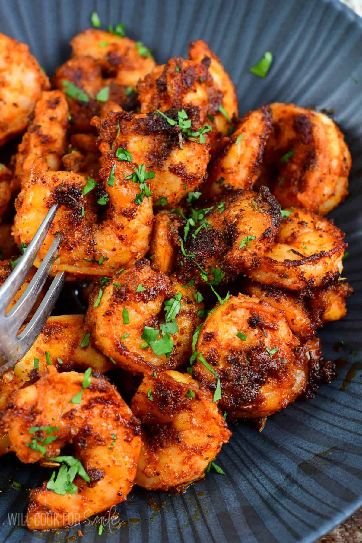 several cooked blackened shrimp in a bowl with a fork.