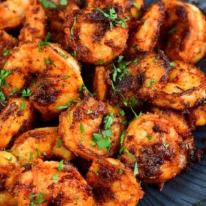 a pound of cooked blackened shrimp in a black bowl with parsley garnish.
