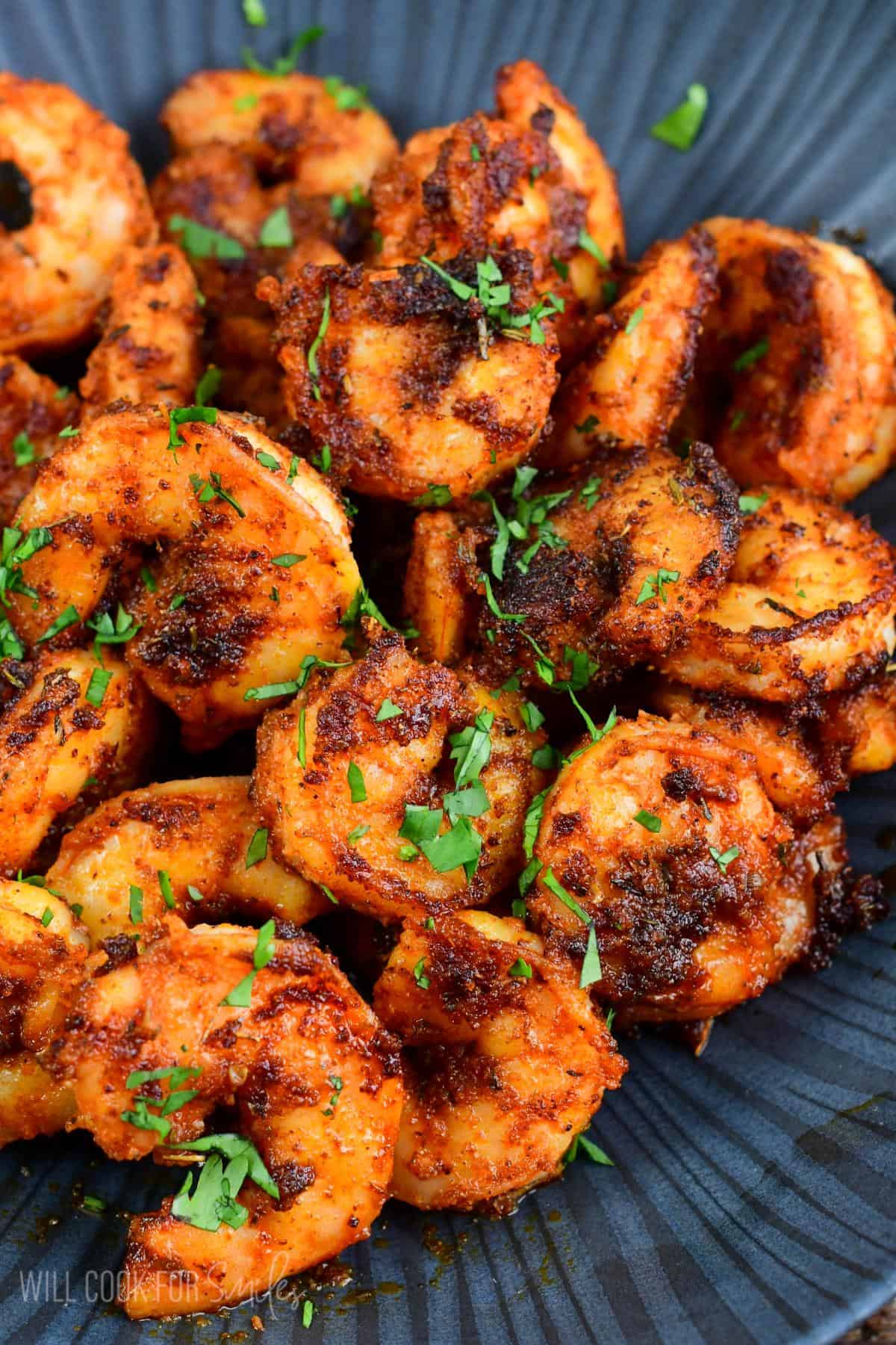 a pound of cooked blackened shrimp in a black bowl with parsley garnish.