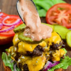 adding creamy burger sauce with a spoon on top of a juicy smashed burger with lettuce, pickle, onion, and cheese.