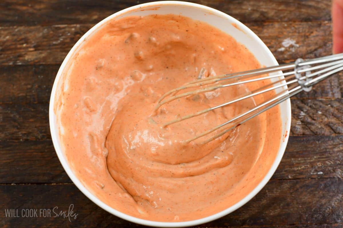 burger sauce being mixed with a whisk in a bowl on a wood surface.