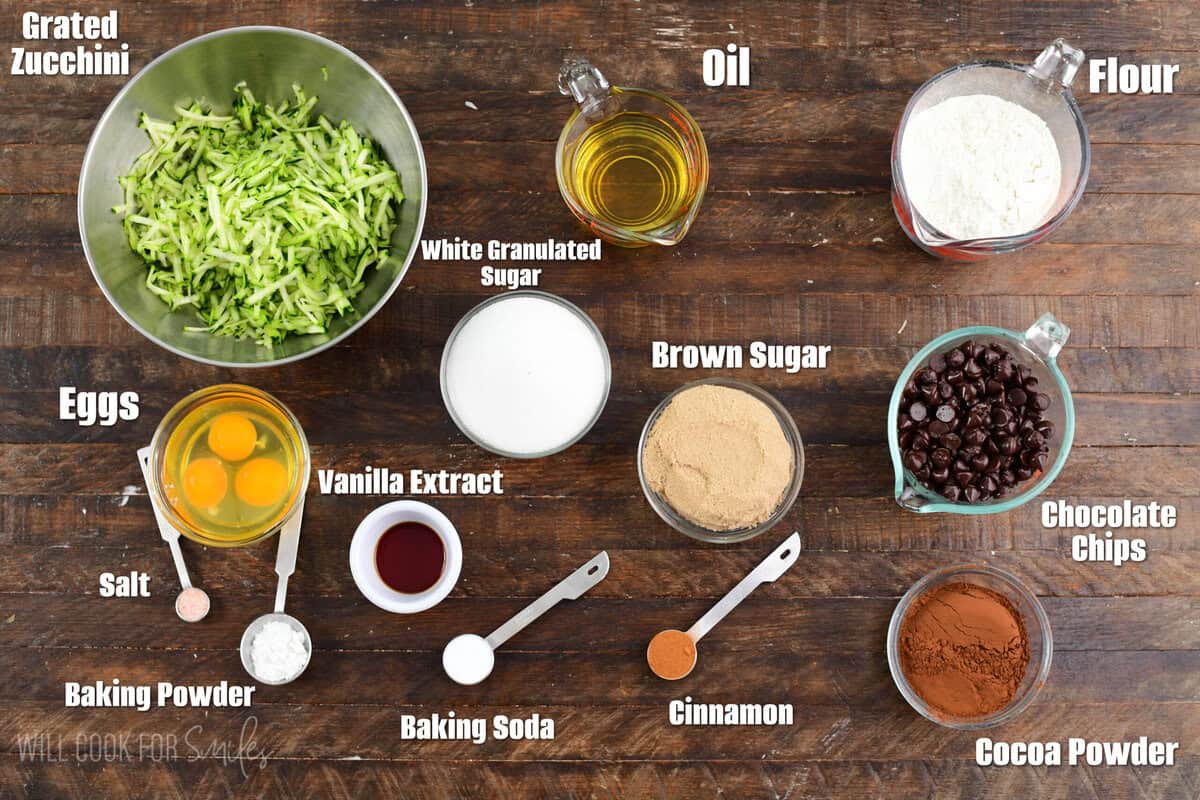 Labeled ingredients for zucchini muffins on a wood surface.
