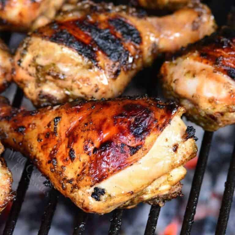 three jerk marinated chicken legs cooking on the charcoal grill.