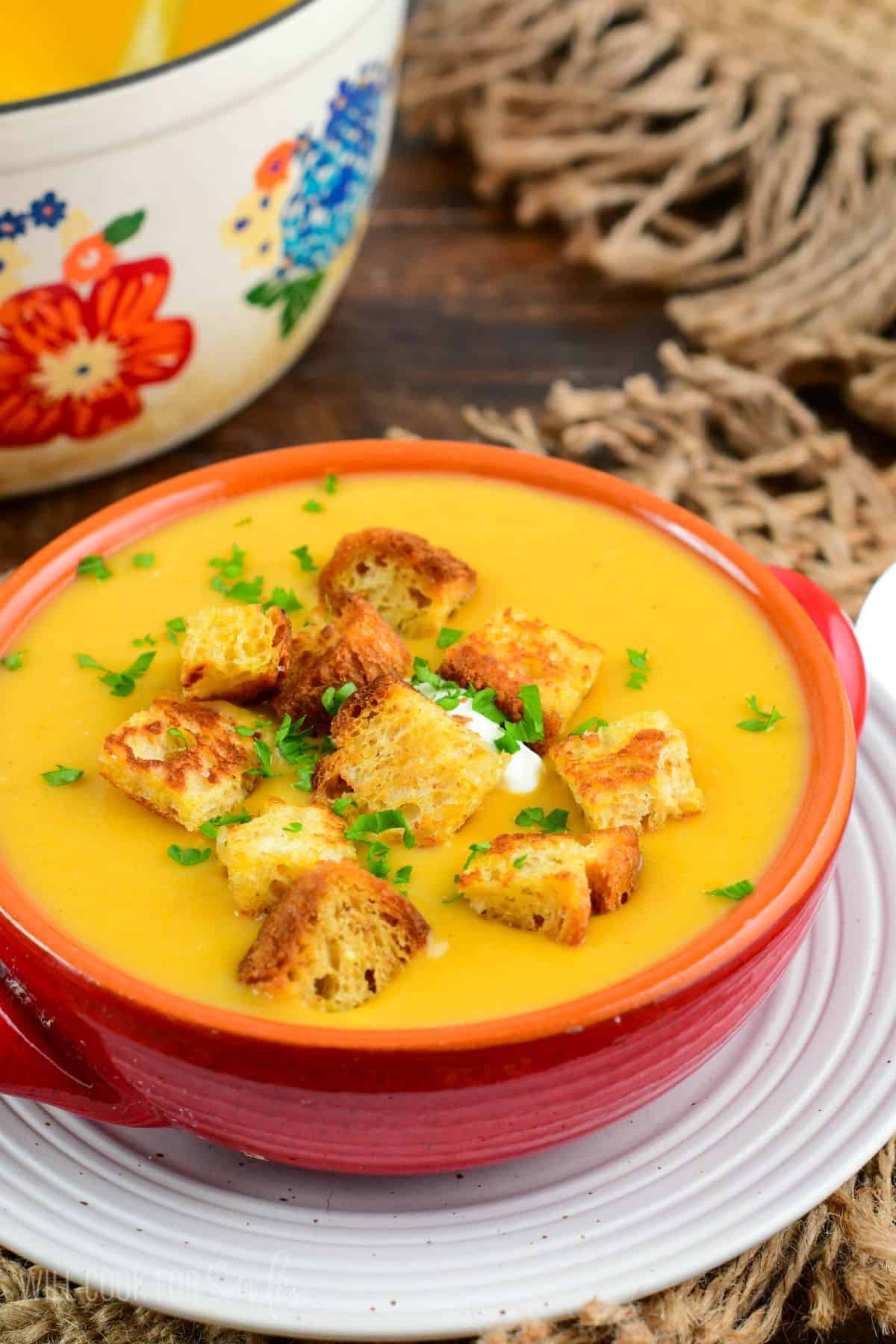 Butternut squash potato soup topped with croutons, parsley, and sour cream in a red bowl.