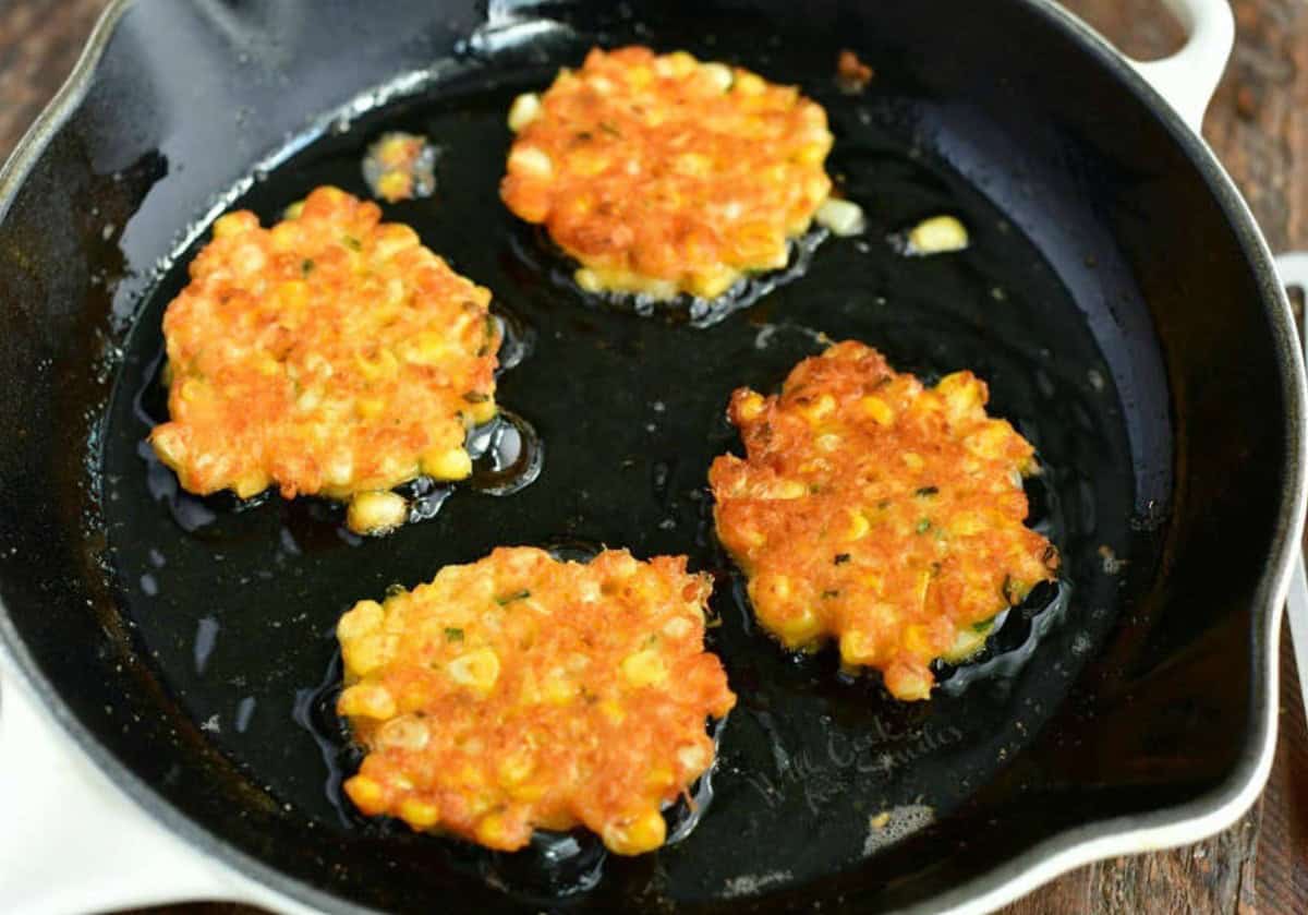 cooking four corn fritters in a cast iron skillet.