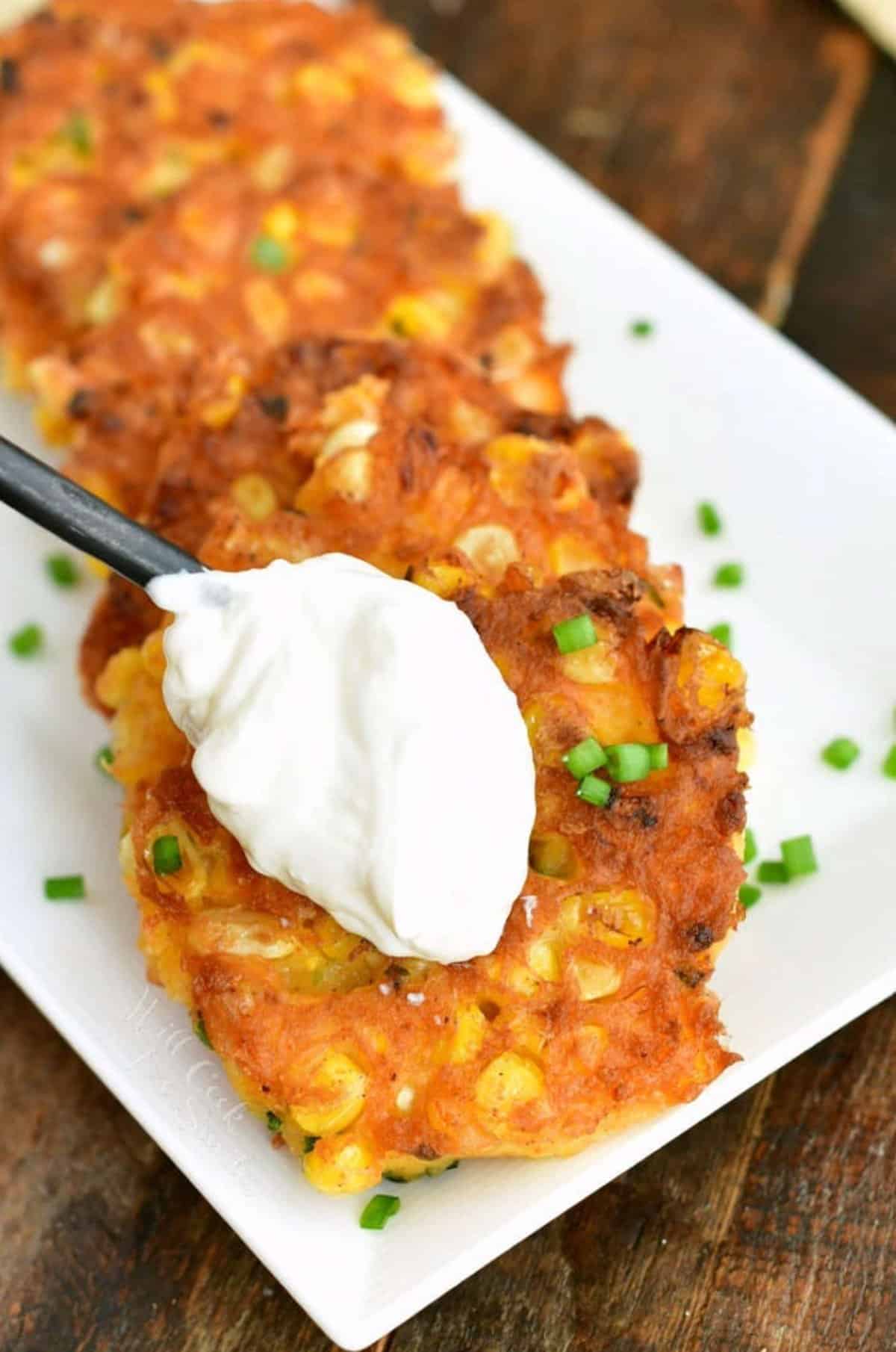 adding a dollop of sour cream onto the corn fritters.