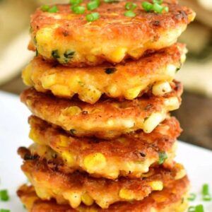 stacked six corn fritters on top of each other with some green onions.