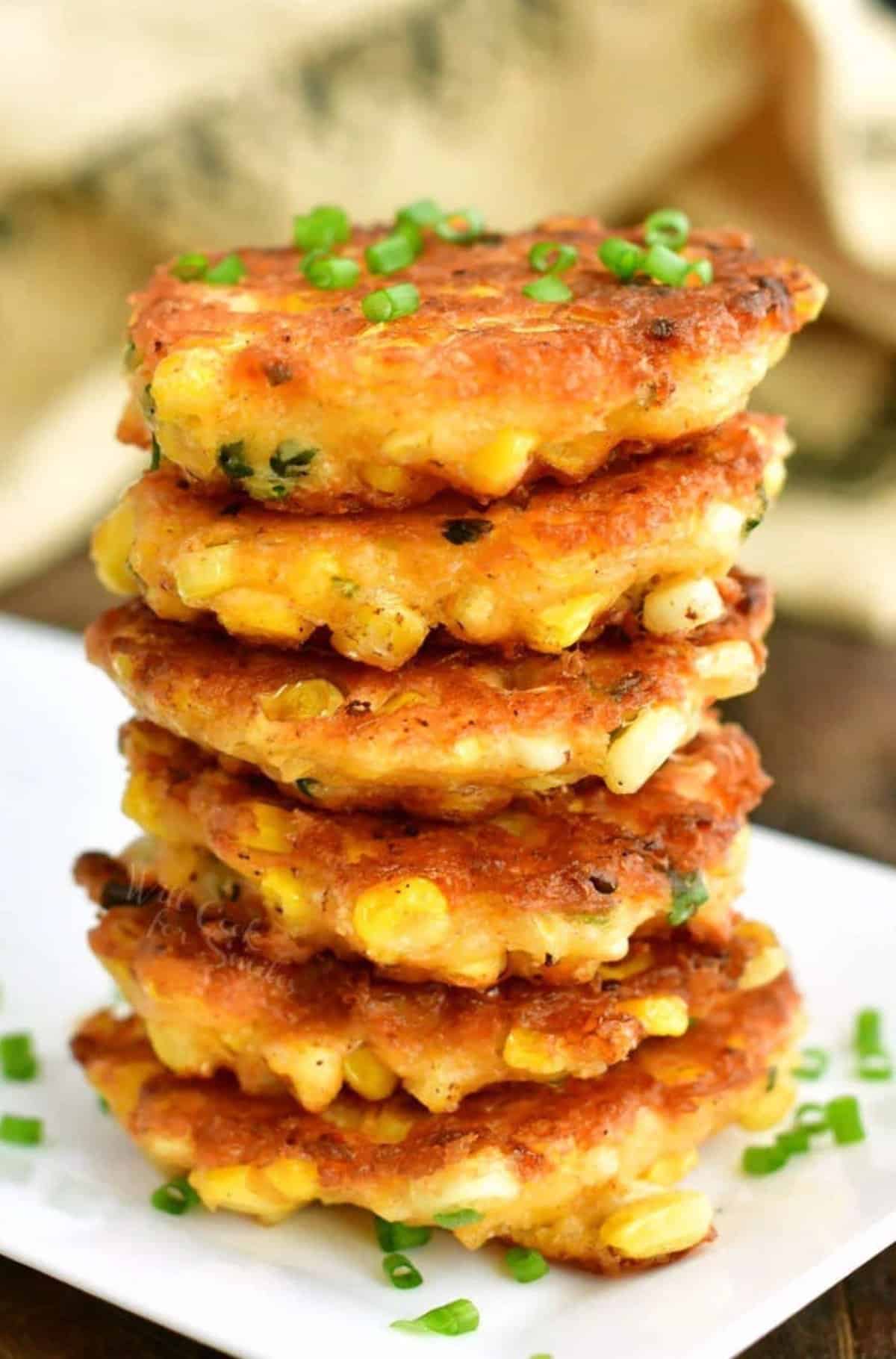 stacked six corn fritters on top of each other with some green onions.