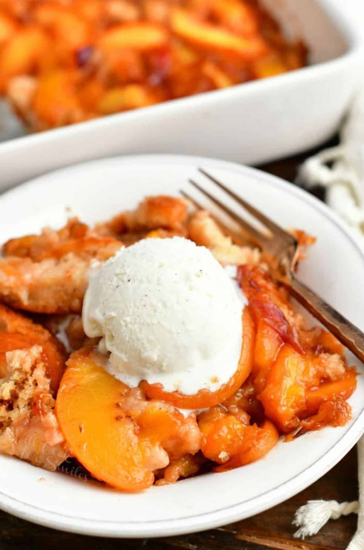 peach cobbler topped with ice cream in a white bowl.