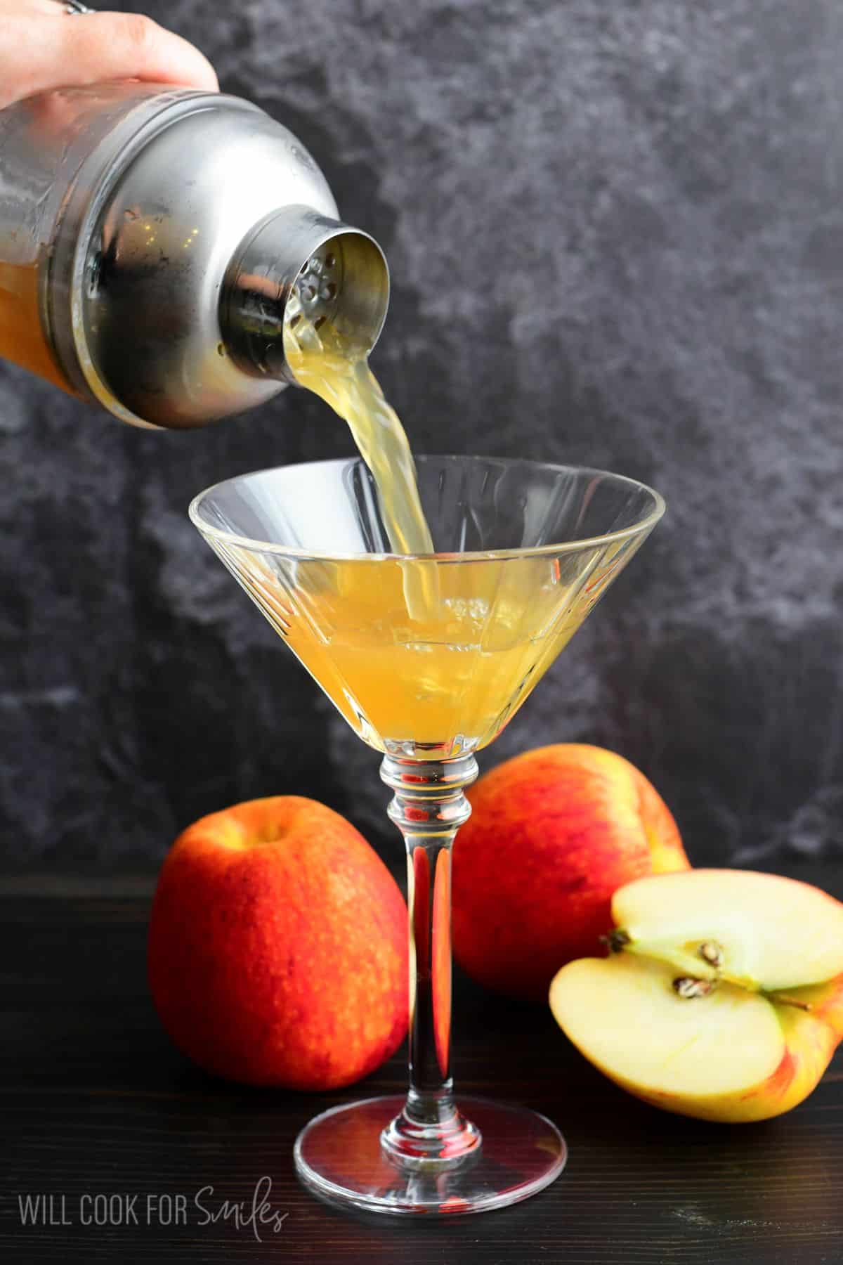 pouring apple cider martini in a martini glass with an apples around stem of glass.