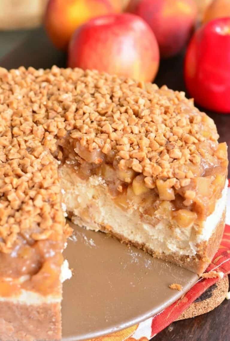 a whole apple cheesecake with a slice taken out next to apples.