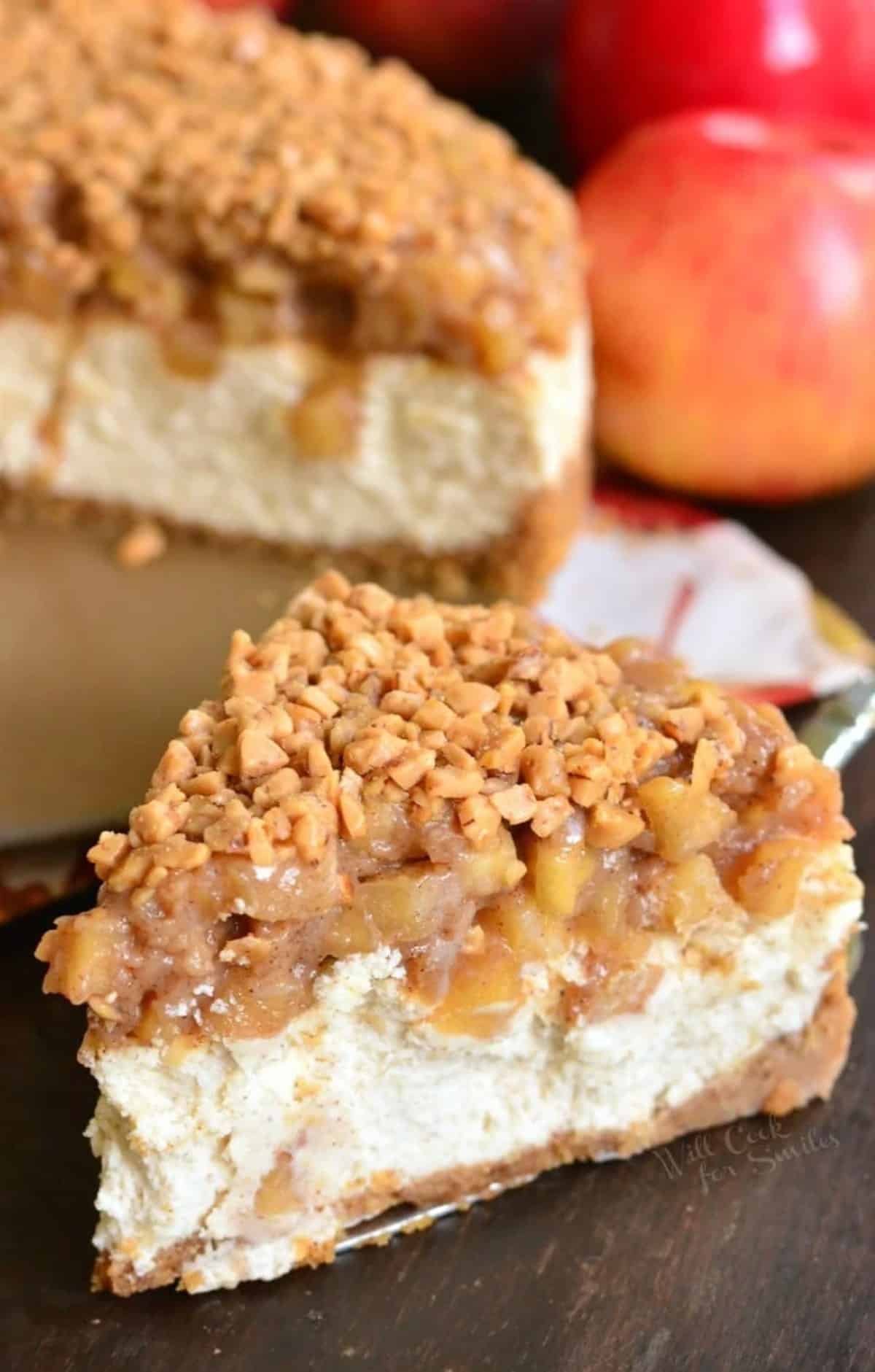 a slice of apple cheesecake with toffee crunch on top next to whole cheesecake.