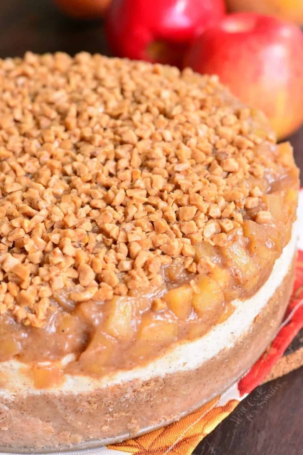 whole apple pie cheesecake topped with toffee crunch and apples around.