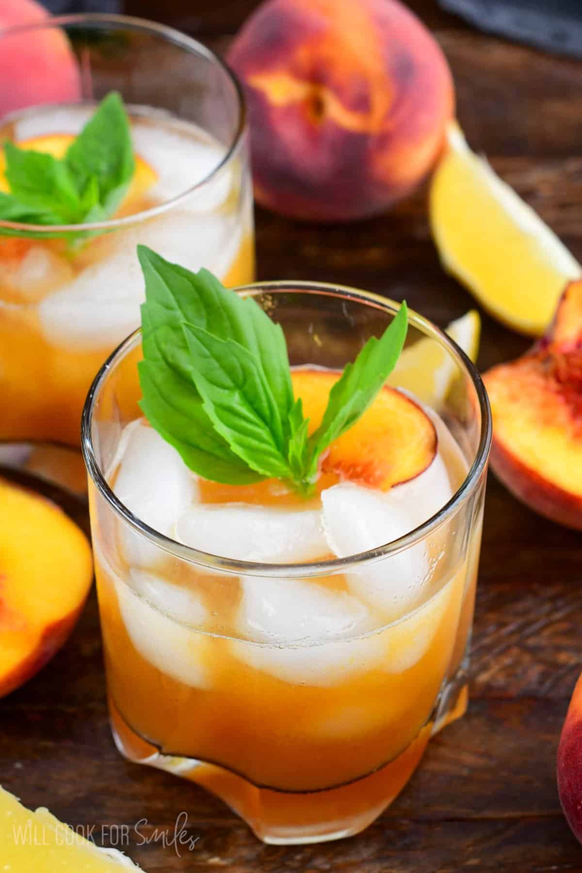 Peach smash bourbon in a glass with ice and peaches and mint on top as garnish.