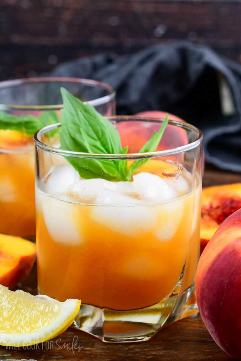 Peach bourbon smash in a glas with mint and peaches on top as garnish.