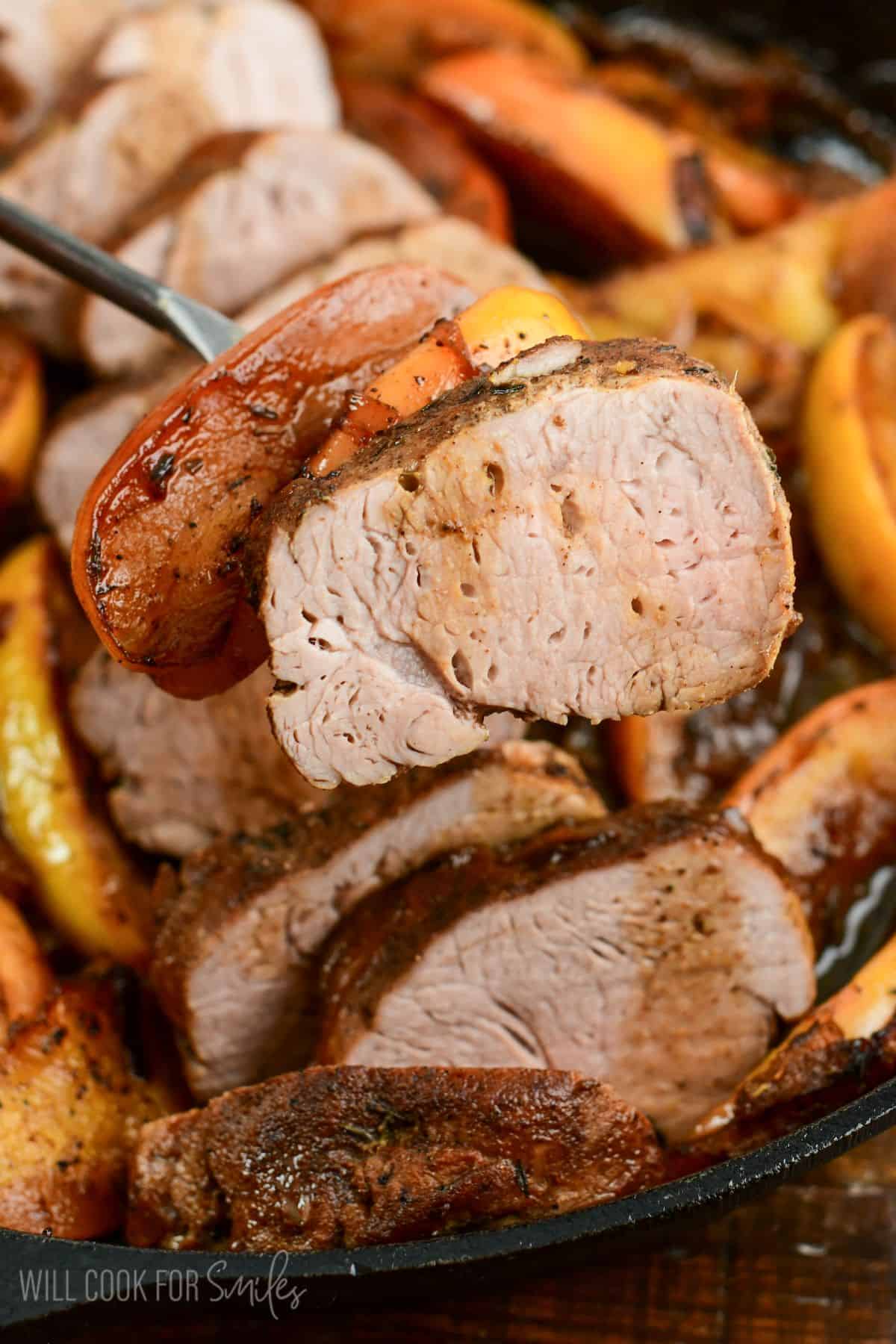 roasted pork and apples in a pan with some of the park and apples on a fork.