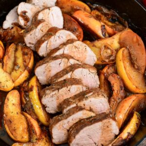 sliced roasted pork with apples in a cast iron skillet.