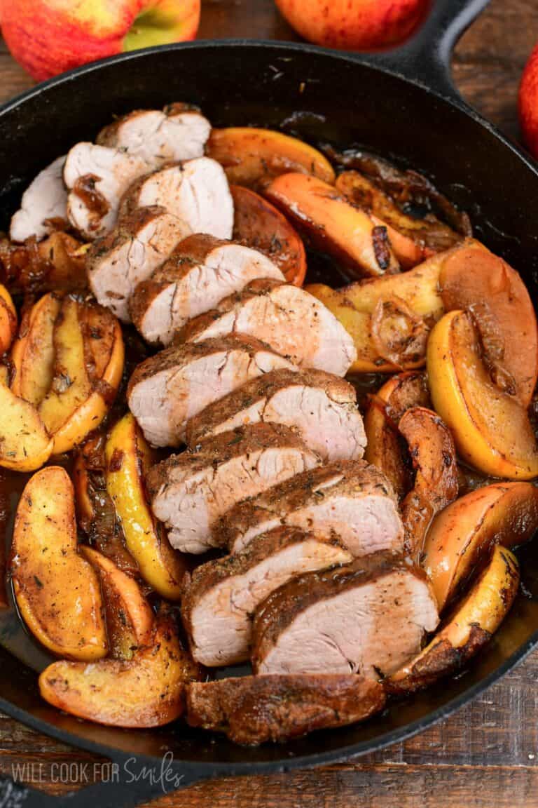 sliced roasted pork with apples in a cast iron skillet.