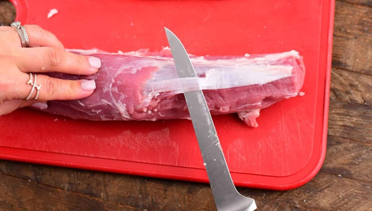Paring knife removing silverskin from a raw pork tenderloin.