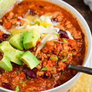 scooping out some turkey chili from a bowl with a metal spoon.