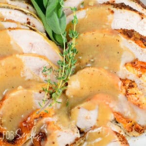 Sliced roasted turkey breast topped with golden gravy and herbs, served on a holiday white platter for Thanksgiving dinner.