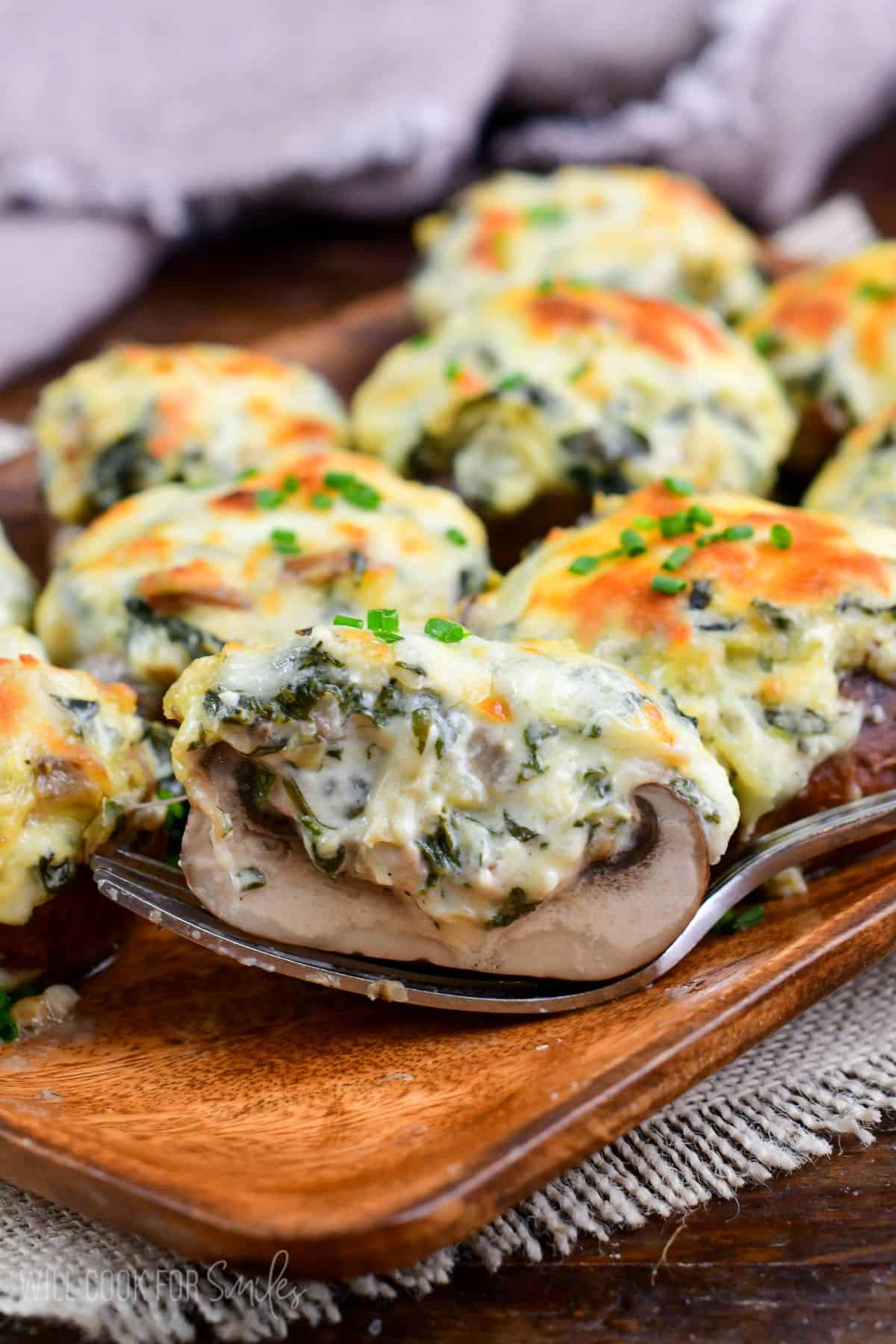 holding half of a creamy and cheesy spinach artichoke stuffed mushroom with melted golden cheese on top.