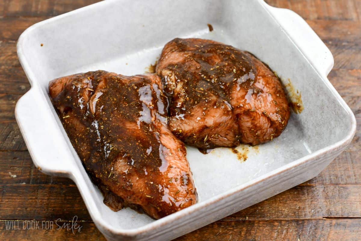 two turkey tenderloin breasts in a rich and flavorful balsamic marinade mixture in a baking dish.