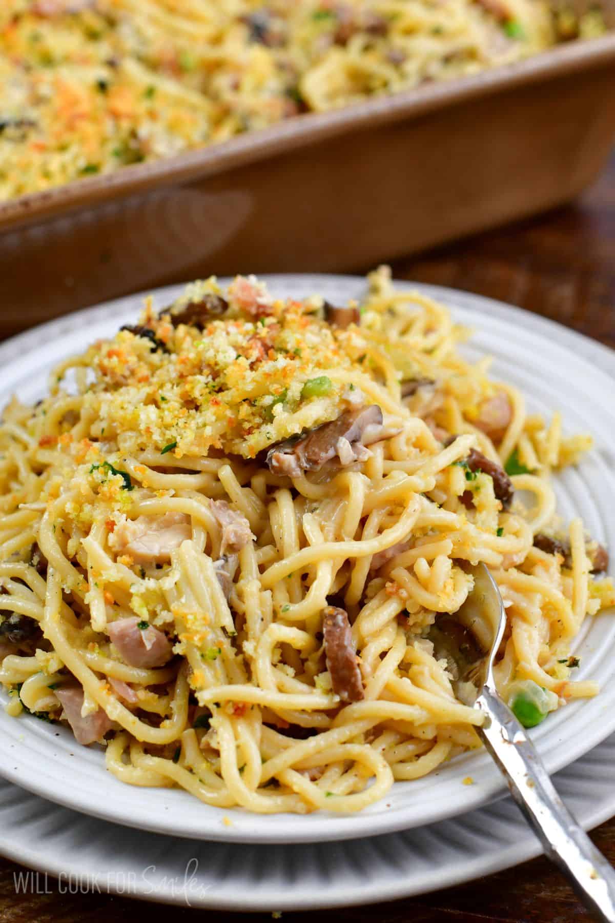 Turkey tetrazzini on a plate with a fork and the casserole dish in the background.