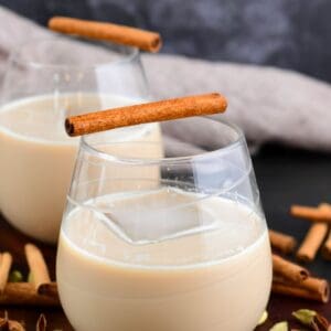 creamy chai cocktail in a glass with an ice cube and cinnamon stick.