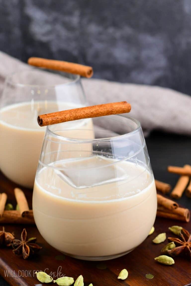 creamy chai cocktail in a glass with an ice cube and cinnamon stick.