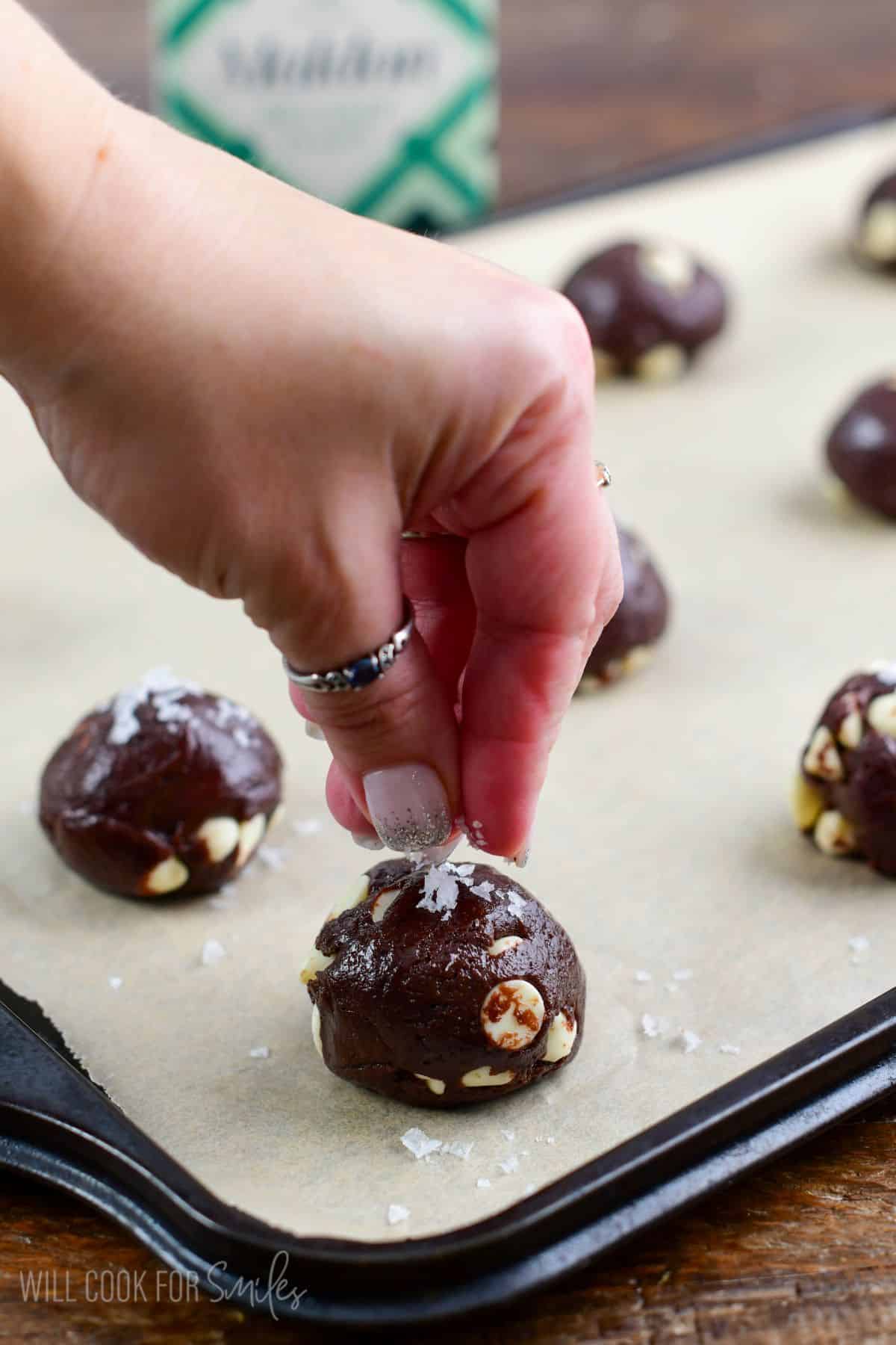 Chocolate brown butter cookie dough on parchments lined baking sheet adding course salt.