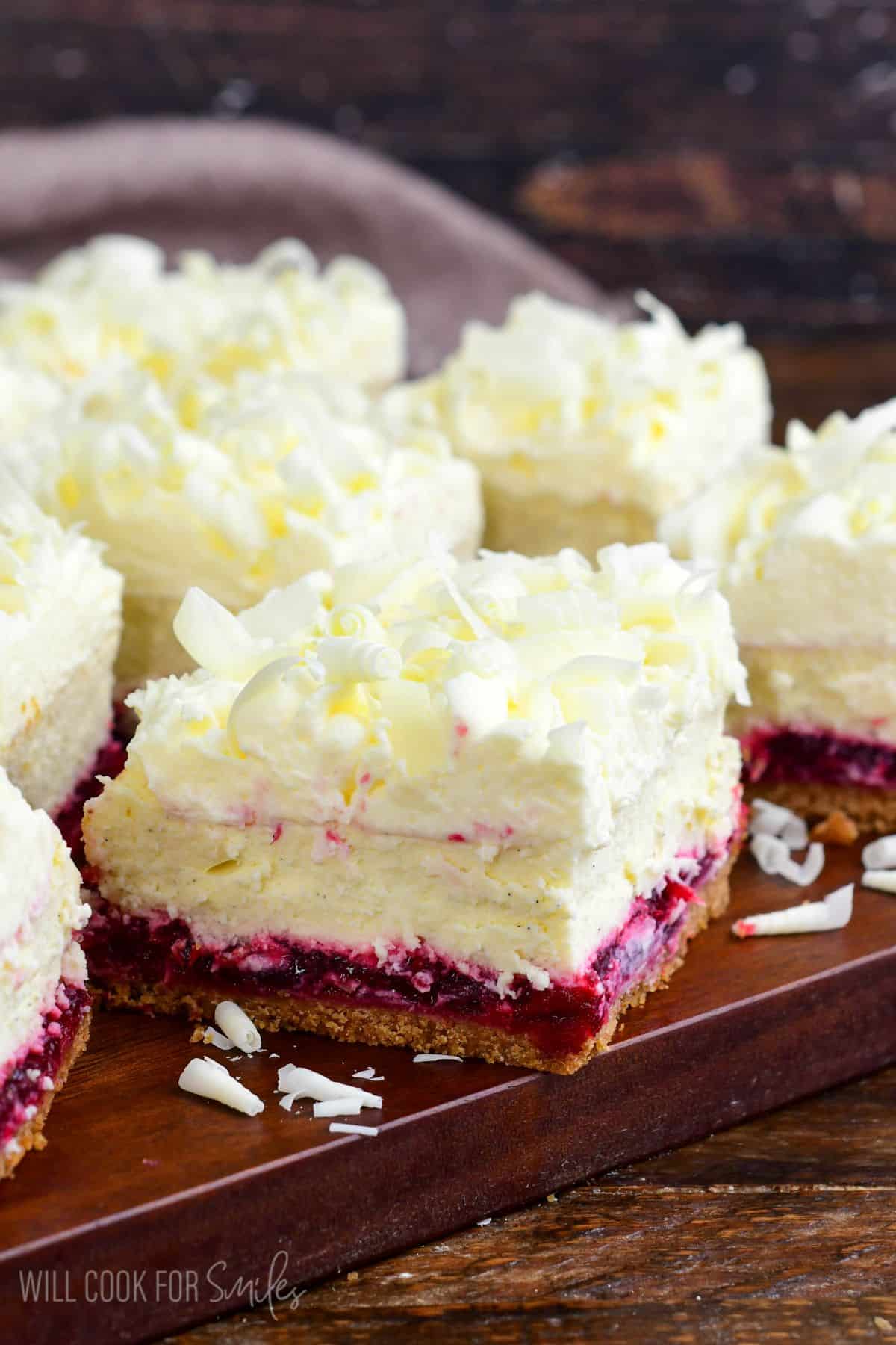 Cut Christmas cheesecake bars with white chocolate shavings on a wood surface.