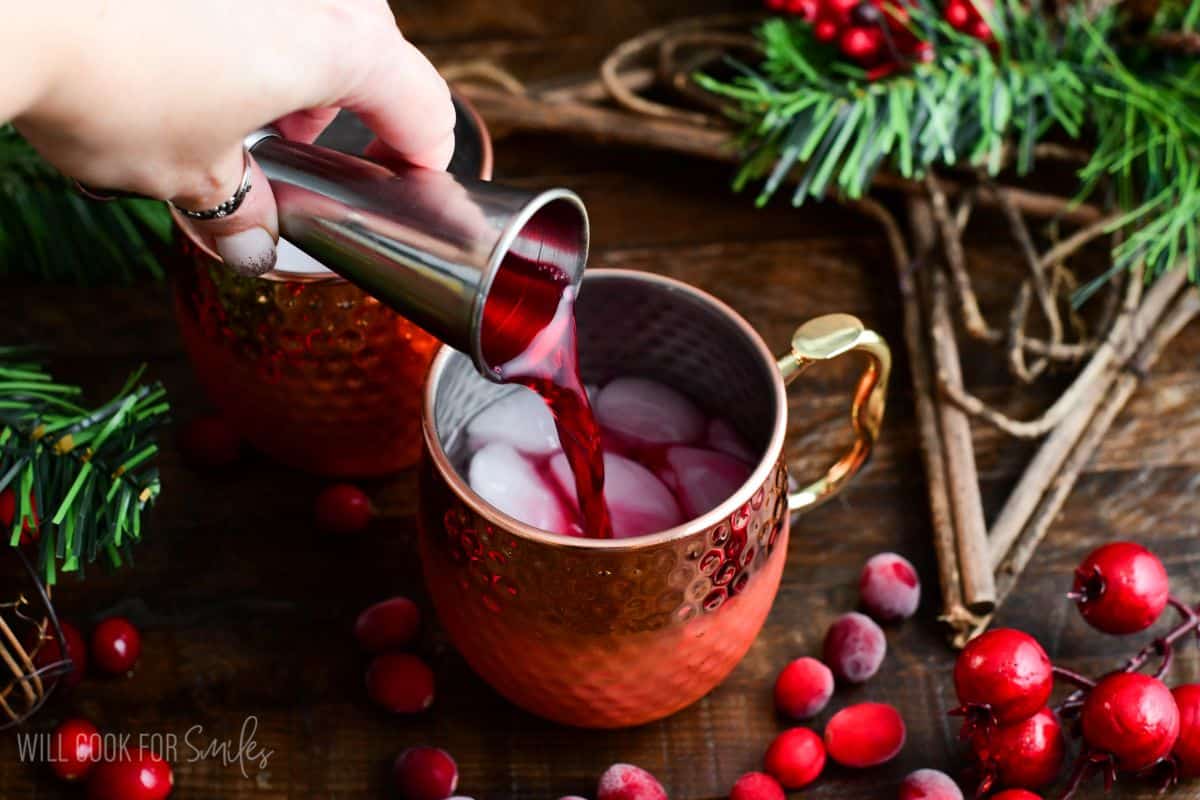 Adding cranberry to a copper mug with the vodka ice on a wood surface with cranberries.